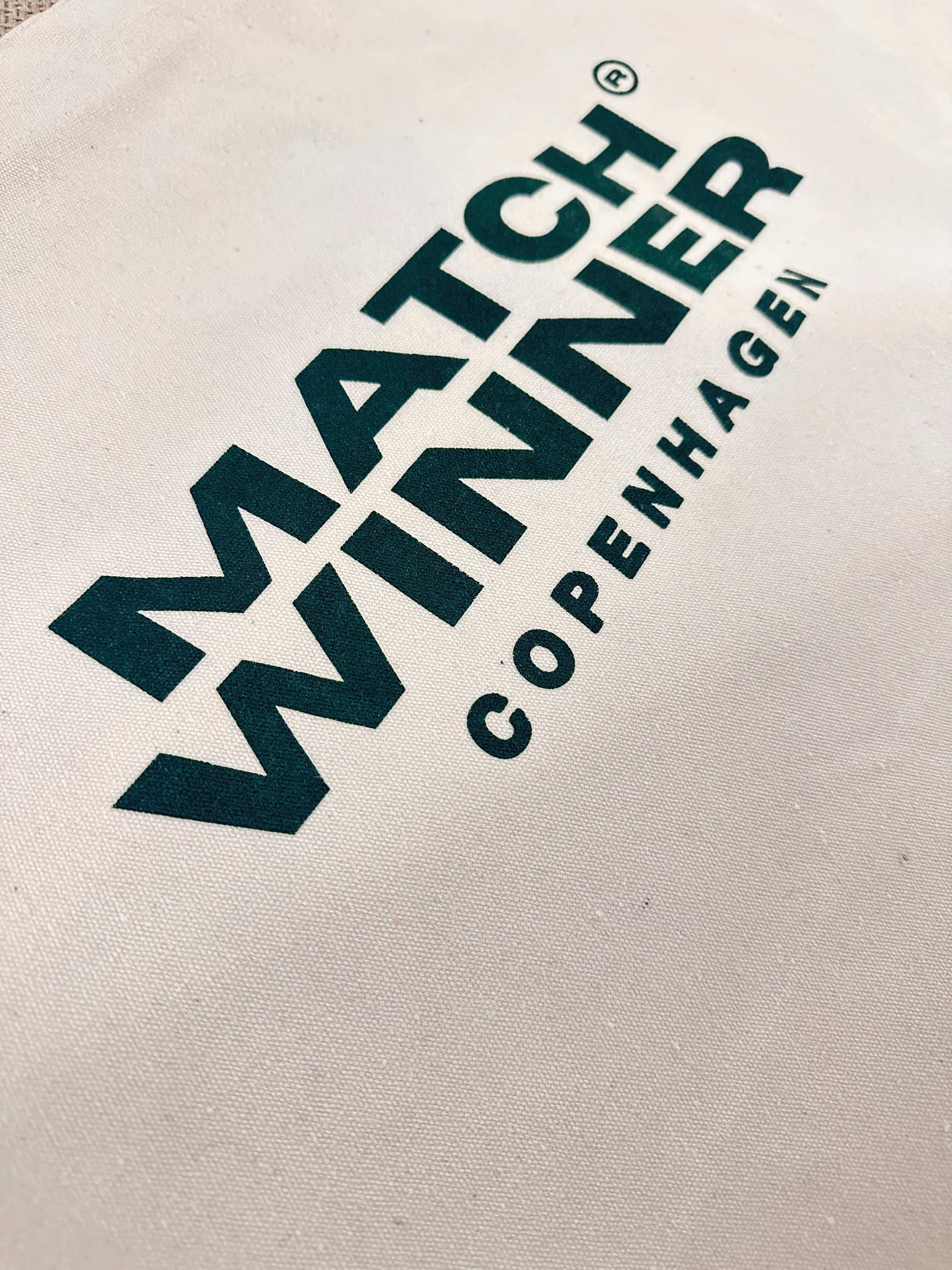 Nærbillede af det mørkegrønne Matchwinner Copenhagen logo trykt på en PREMIUM MW TOTEBAG mulepose.