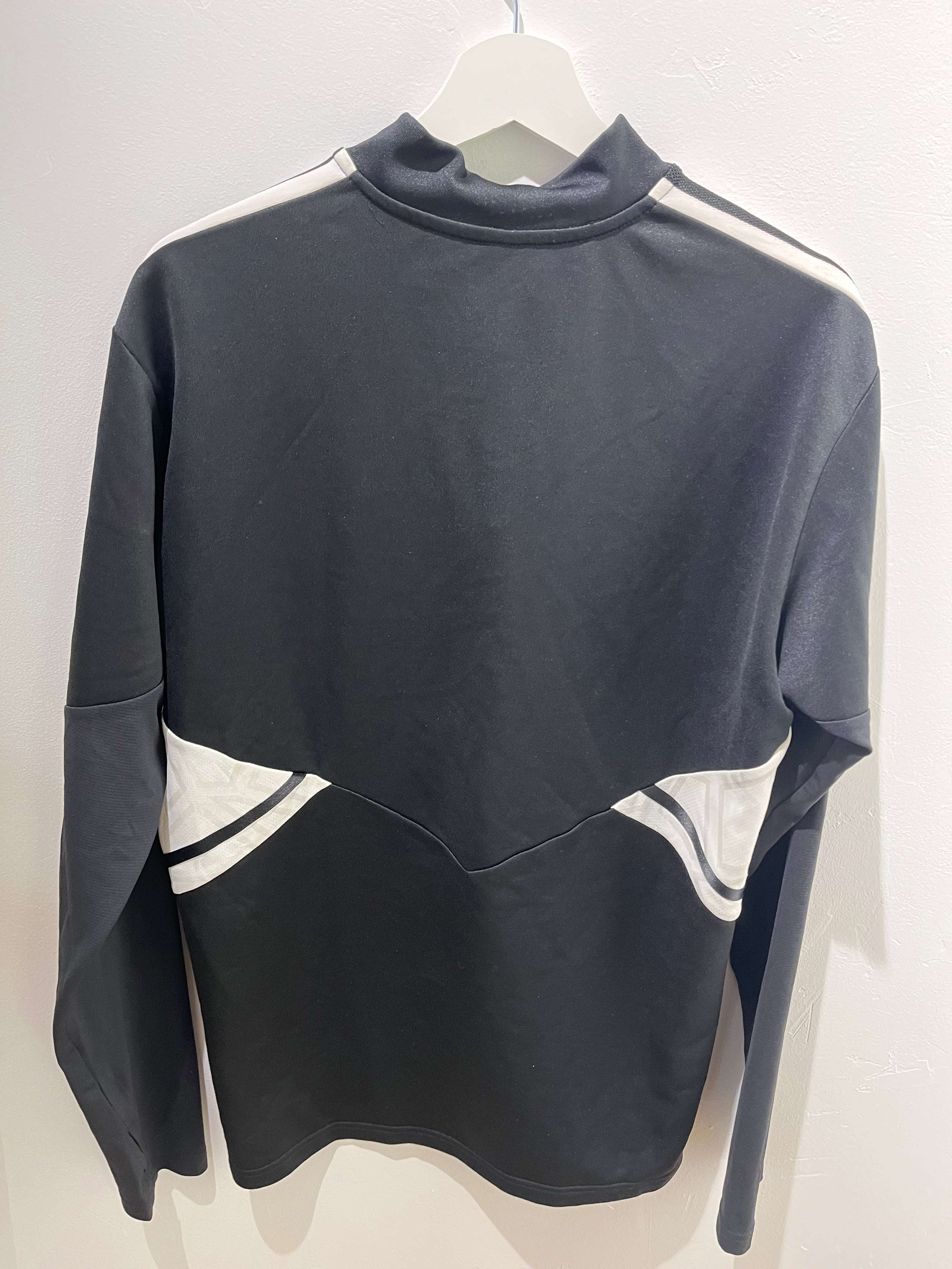 Bagsiden af en sort og hvid FCK Træningsovertrøje L på en hvid bøjle fra Matchwinner.